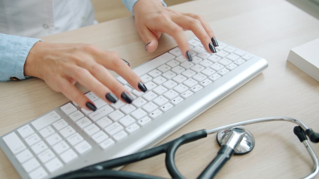 Doctor's hands typing on a computer keyboard at a desk, representing the administrative side of NHS work and pension record-keeping