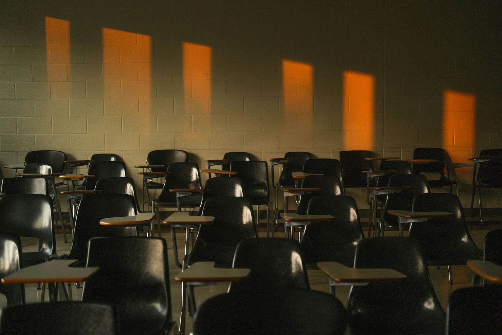 Empty classroom with rows of desks and warm sunlight streaming through tall windows