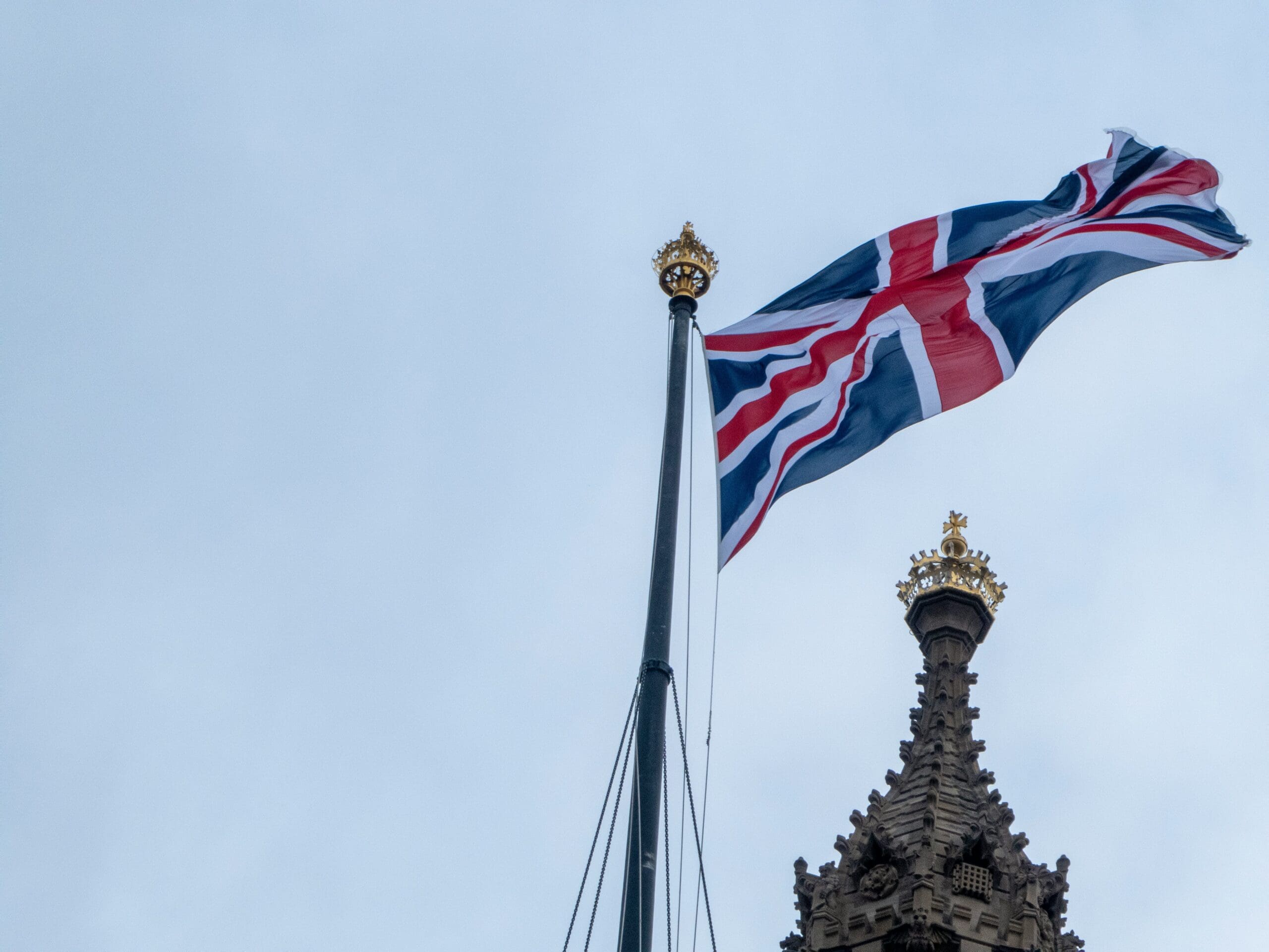 The Union Jack flag flying above the Houses of Parliament in Westminster, London, against a bright sky