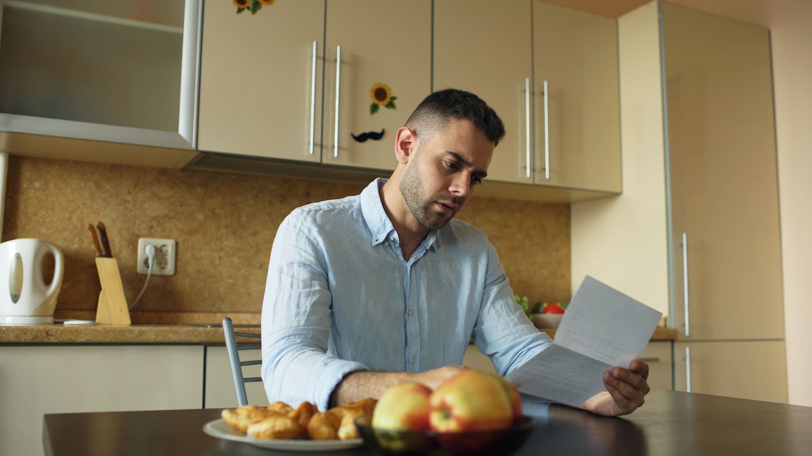 Person at a kitchen table reading a letter and reviewing paperwork